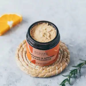 Organic orange and carrot body scrub in a jar on a marble surface.