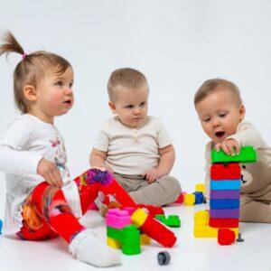 Drei Kinder spielen mit bunten Weiche Bausteine im weißen Raum.