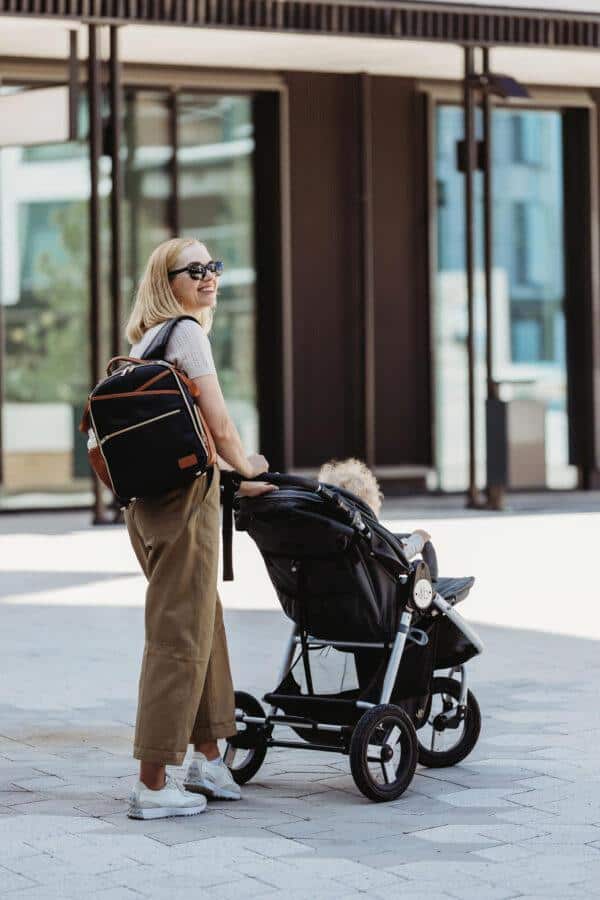 Woman with a diaper backpack and stroller in an urban setting.