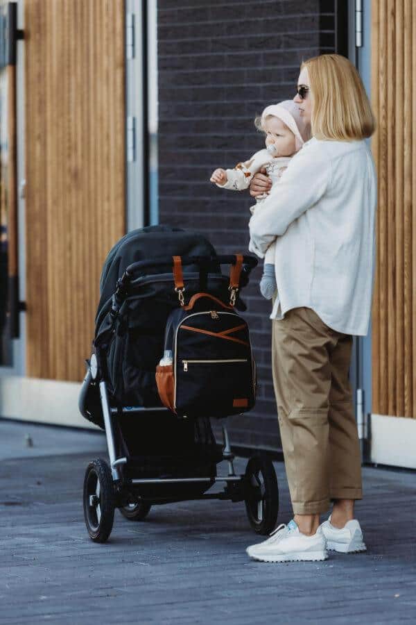 Mother with baby and small diaper backpack in urban setting.