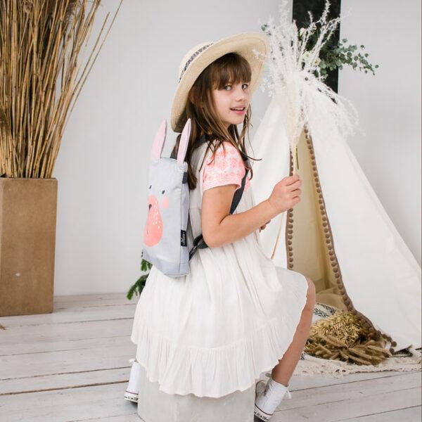 Kids backpack with bunny design worn by a girl in a white dress and hat.