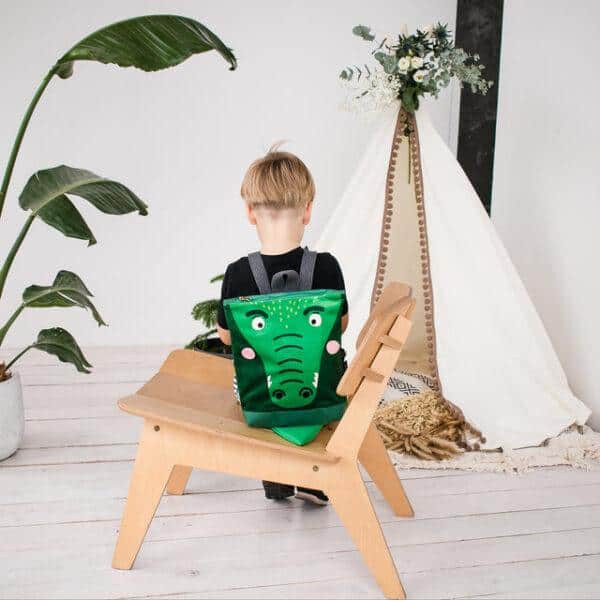Kids backpack with crocodile design on a wooden chair in a modern room.