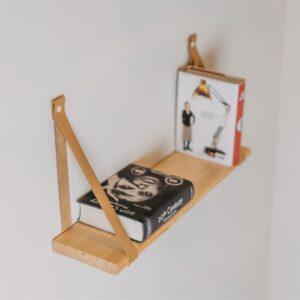 Floating wooden shelf with leather straps holding books and a magazine.
