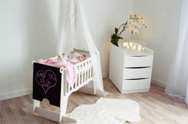 Baby cradle with pink blanket and stuffed animals in a nursery room.