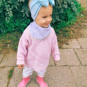 Adorable toddler wearing light blue headband and pink scarf bib outdoors.