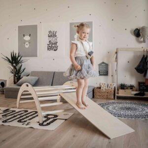 Kleines Mädchen auf Montessori-Kletterbogen mit Rampe in Spielzimmer.