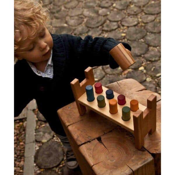 Child playing with colorful wooden pounding bench outdoors.