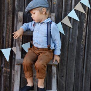 Child sitting on a ladder wearing vintage-style outfit and a flat cap.